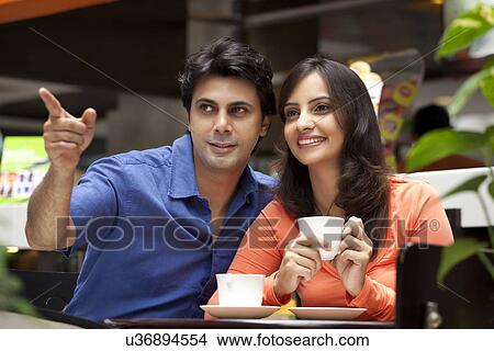Picture - Man showing something to wife while having tea in shopping mall . Fotosearch