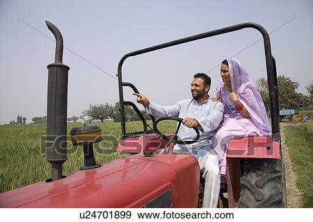 Stock Photo - Man showing something to wife while driving a tractor . Fotosearch