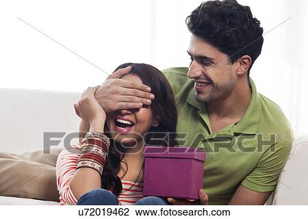 Stock Image - Man surprising a woman with a gift. Fotosearch