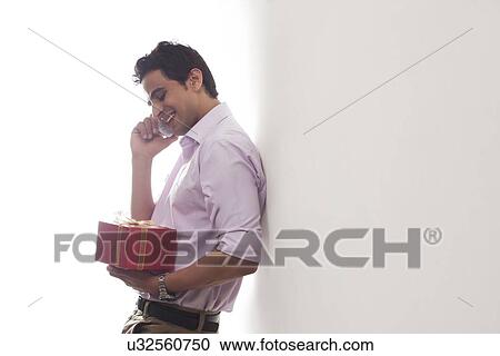 Stock Image - Man with a gift talking on a mobile phone. Fotosearch