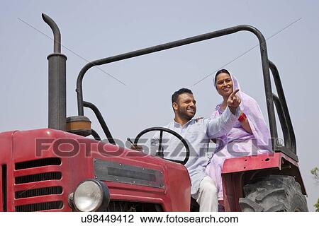 Stock Image - Mid adult couple on a tractor with man pointing at something . Fotosearch