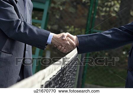 Midsection of businessmen shaking hands over tennis net in court View Large Photo Image Stock Image - Midsection of businessmen shaking hands over tennis net in court . Fotosearch