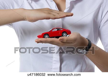 Stock Image - Midsection of insurance agent covering toy car against white background. Fotosearch
