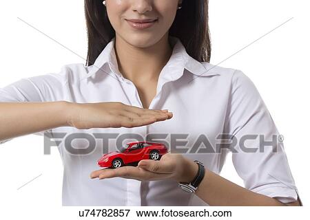 Stock Photo - Midsection of young female insurance agent holding toy car against white background. Fotosearch