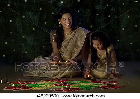 Stock Image - Mother and daughter arranging diyas . Fotosearch