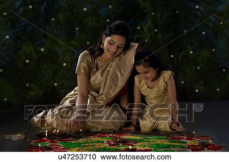 Stock Image - Mother and daughter arranging diyas . Fotosearch