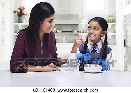 Stock Image - Mother and daughter looking at each other while girl having breakfast . Fotosearch