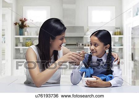 Mother feeding daughter breakfast at home View Large Photo Image Stock Photograph - Mother feeding daughter breakfast at home . Fotosearch