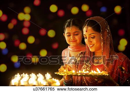 Mother holding a tray of diyas while her daughter looks on View Large Photo Image Stock Photography - Mother holding a tray of diyas while her daughter looks on . Fotosearch