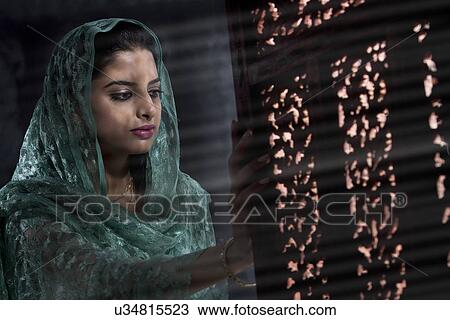 Stock Image - Muslim woman looking out of a window . Fotosearch