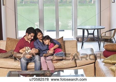 Stock Photo - Parents sitting together with kids on sofa at home . Fotosearch