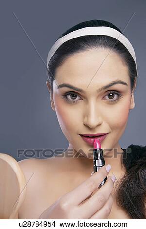 Picture - Portrait of a beautiful female applying lipstick over colored background . Fotosearch