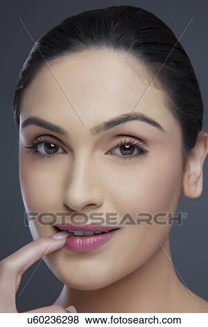 Stock Photo - Portrait of a beautiful young woman biting fingernail over colored background . Fotosearch