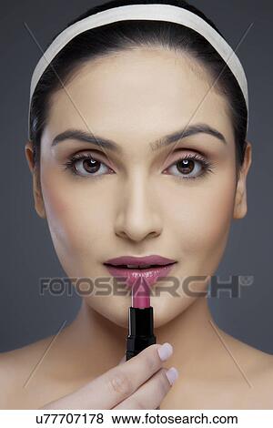 Portrait of a beautiful young woman holding lipstick over colored background View Large Photo Image Stock Photo - Portrait of a beautiful young woman holding lipstick over colored background . Fotosearch