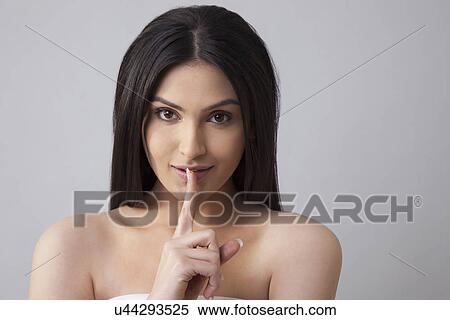 Stock Photography - Portrait of a beautiful young woman with finger on lips over colored background . Fotosearch