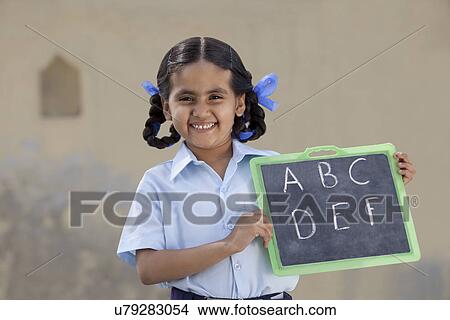 Portrait of a cheerful girl in school uniform holding a slate View Large Photo Image Picture - Portrait of a cheerful girl in school uniform holding a slate . Fotosearch