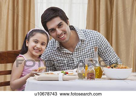 Stock Image - Portrait of a happy father and daughter having pizza at restaurant . Fotosearch