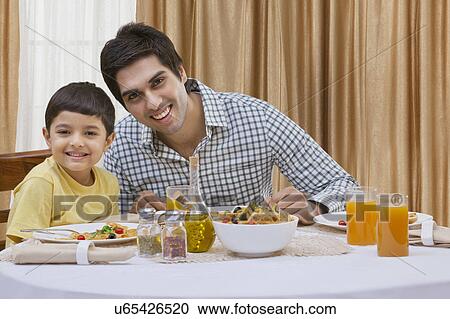 Stock Image - Portrait of a happy father and son having pizza at table . Fotosearch