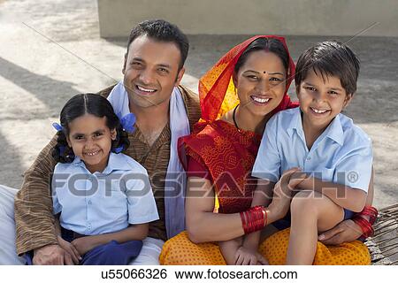 Stock Photograph - Portrait of a happy Indian family of four sitting on cot . Fotosearch