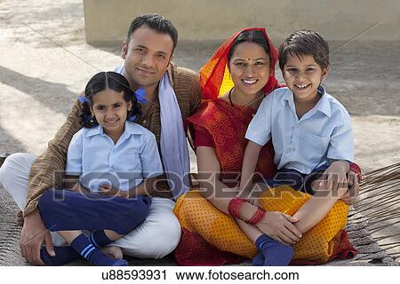 Stock Image - Portrait of a happy Indian family sitting on cot . Fotosearch