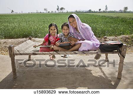 Stock Photo - Portrait of a happy mother sitting with her kids on cot . Fotosearch