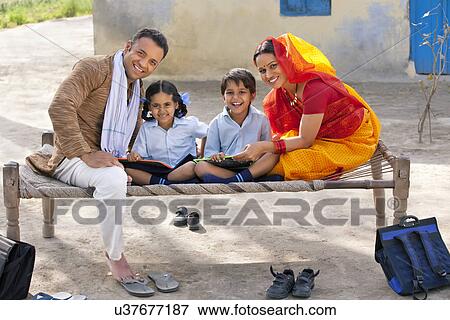 Stock Photo - Portrait of a happy rural family of four sitting on cot . Fotosearch