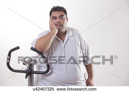 Portrait of a lazy obese man with an exercise bike over white background View Large Photo Image Stock Photography - Portrait of a lazy obese man with an exercise bike over white background . Fotosearch