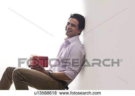 Portrait of a man holding a gift leaning against wall View Large Photo Image Stock Photo - Portrait of a man holding a gift leaning against wall. Fotosearch