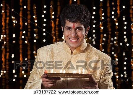 Stock Image - Portrait of a man holding a tray of diyas. Fotosearch