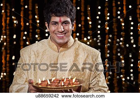 Portrait of a man holding a tray of diyas View Large Photo Image Stock Image - Portrait of a man holding a tray of diyas. Fotosearch