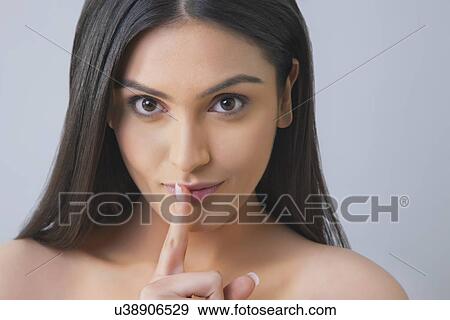 Stock Photo - Portrait of a pretty young woman gesturing finger on lips over colored background . Fotosearch