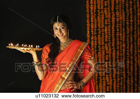 Stock Image - Portrait of a woman holding a tray of diyas. Fotosearch
