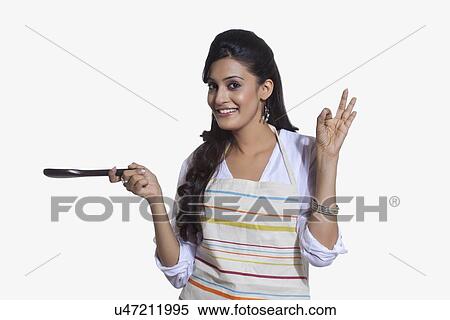 Stock Photography - Portrait of a woman with a cooking utensil giving ok sign. Fotosearch