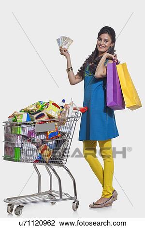 Stock Image - Portrait of a woman with a shopping cart, shopping bags and currency. Fotosearch
