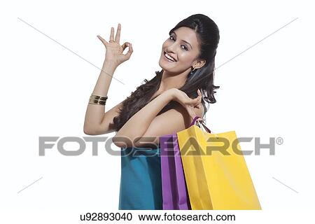 Stock Image - Portrait of a woman with shopping bags giving ok sign. Fotosearch