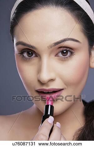 Portrait of a young female applying lipstick over colored background View Large Photo Image Stock Image - Portrait of a young female applying lipstick over colored background . Fotosearch