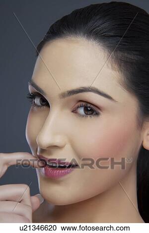Stock Image - Portrait of a young female biting her fingernail over colored background . Fotosearch