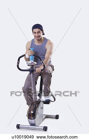 Stock Photo - Portrait of a young man exercising while holding water bottle over white background . Fotosearch