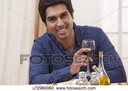 Portrait of a young man holding a glass of wine at restaurant View Large Photo Image Stock Image - Portrait of a young man holding a glass of wine at restaurant . Fotosearch