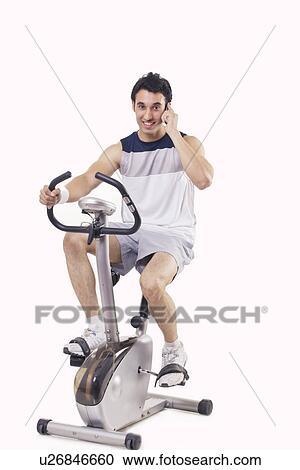 Portrait of a young man talking on mobile phone while exercising over white background View Large Photo Image Stock Image - Portrait of a young man talking on mobile phone while exercising over white background . Fotosearch