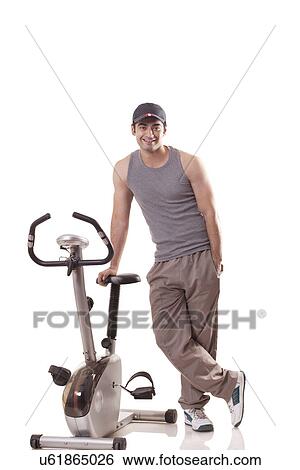 Portrait of a young man with hand in pocket standing next to an exercise bike over white background View Large Photo Image Stock Photograph - Portrait of a young man with hand in pocket standing next to an exercise bike over white background . Fotosearch