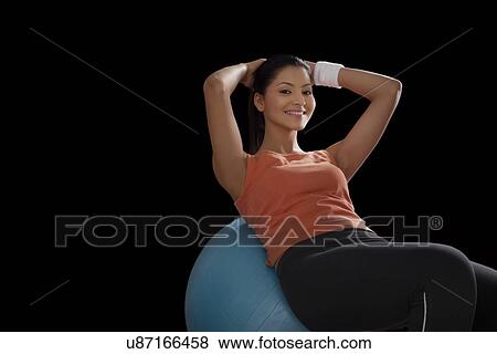 Stock Photo - Portrait of a young woman doing abdominal exercise on a fitness ball over black background . Fotosearch