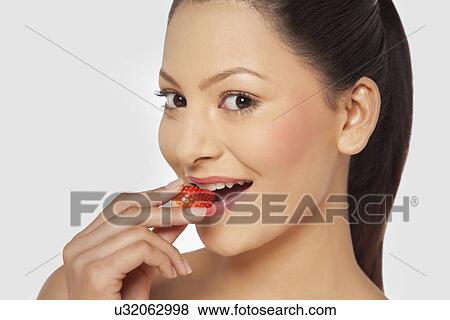 Stock Photo - Portrait of a young woman eating a strawberry . Fotosearch