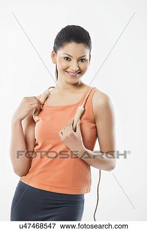 Stock Photo - Portrait of a young woman in sportswear holding jump rope over white background . Fotosearch