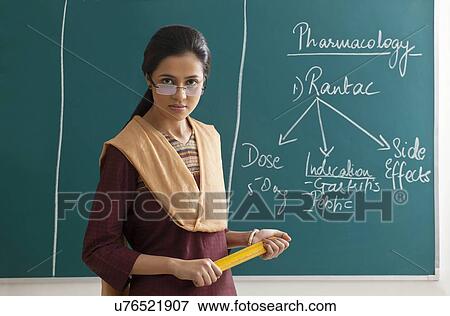 Portrait of an angry female lecturer holding ruler against green board View Large Photo Image Stock Photo - Portrait of an angry female lecturer holding ruler against green board . Fotosearch