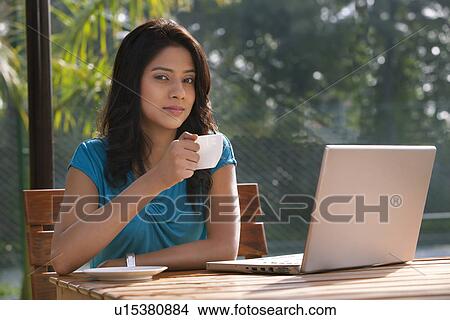 Portrait of an attractive young woman having tea while sitting by table with laptop View Large Photo Image Picture - Portrait of an attractive young woman having tea while sitting by table with laptop . Fotosearch