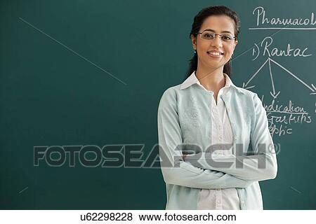 Stock Photo - Portrait of an elementary school teacher with arms crossed standing against green board . Fotosearch