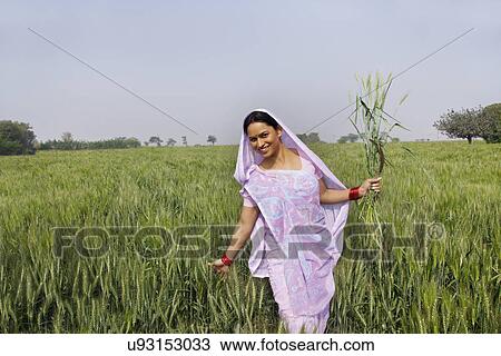 Stock Image - Portrait of an Indian female farm worker gliding through wheat field . Fotosearch