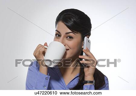 Portrait of beautiful businesswoman using phone while having coffee against gray background View Large Photo Image Stock Image - Portrait of beautiful businesswoman using phone while having coffee against gray background. Fotosearch