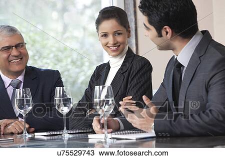 Stock Image - Portrait of beautiful businesswoman smiling while sitting with colleagues in office . Fotosearch